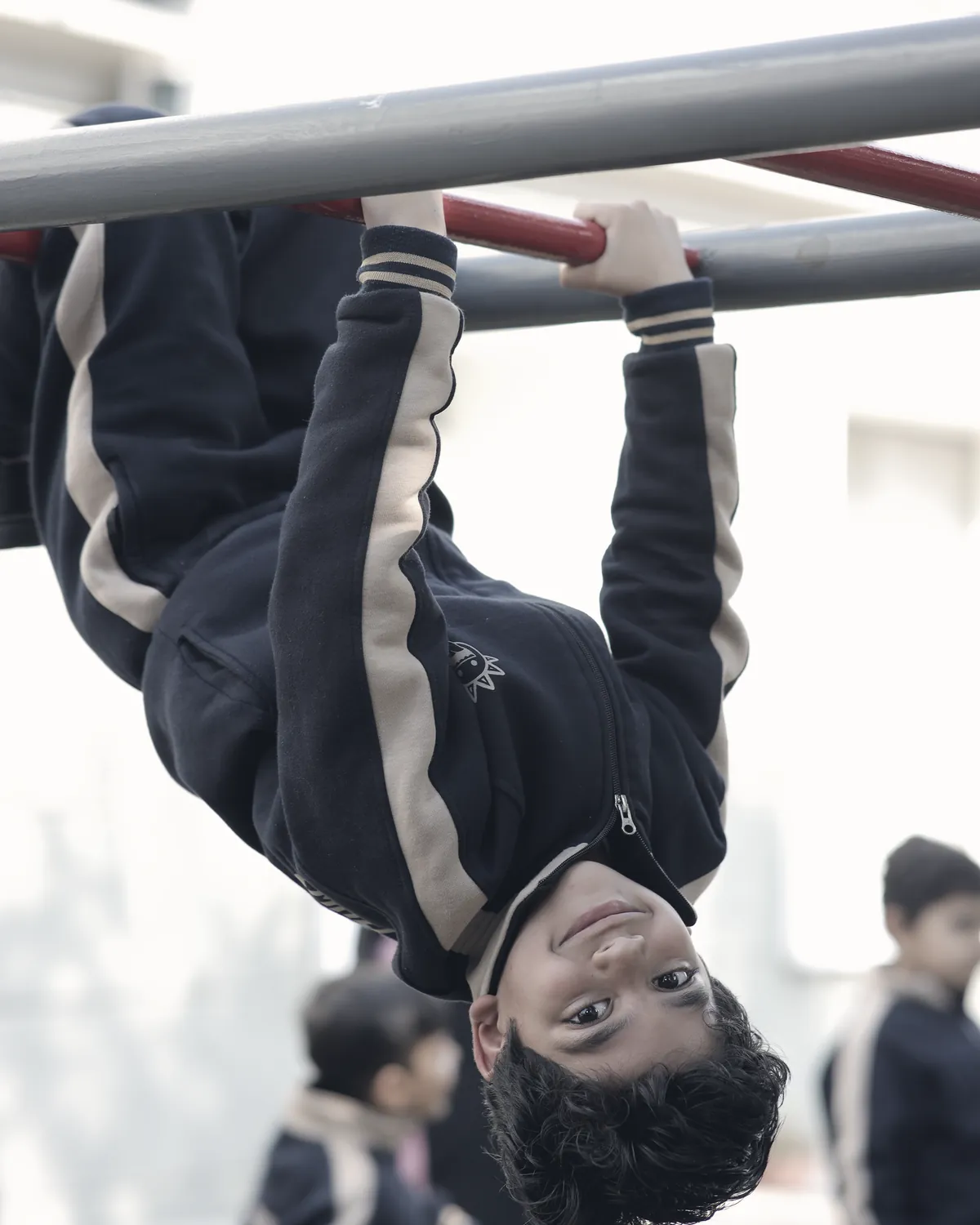 A learner hanging upside down from the bars outside, laughing.